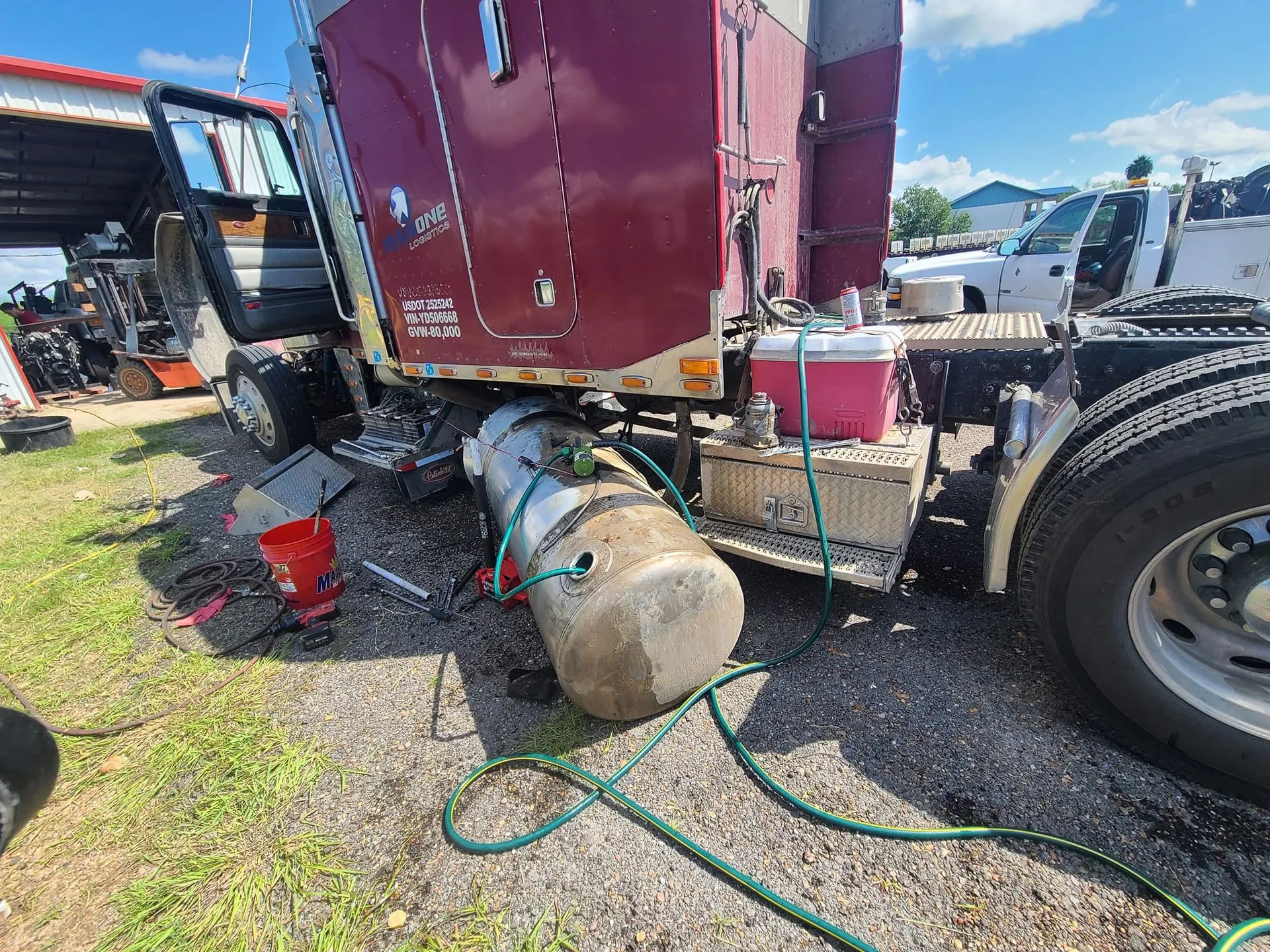 Burgundy semi-truck with a detached fuel tank on the grass.