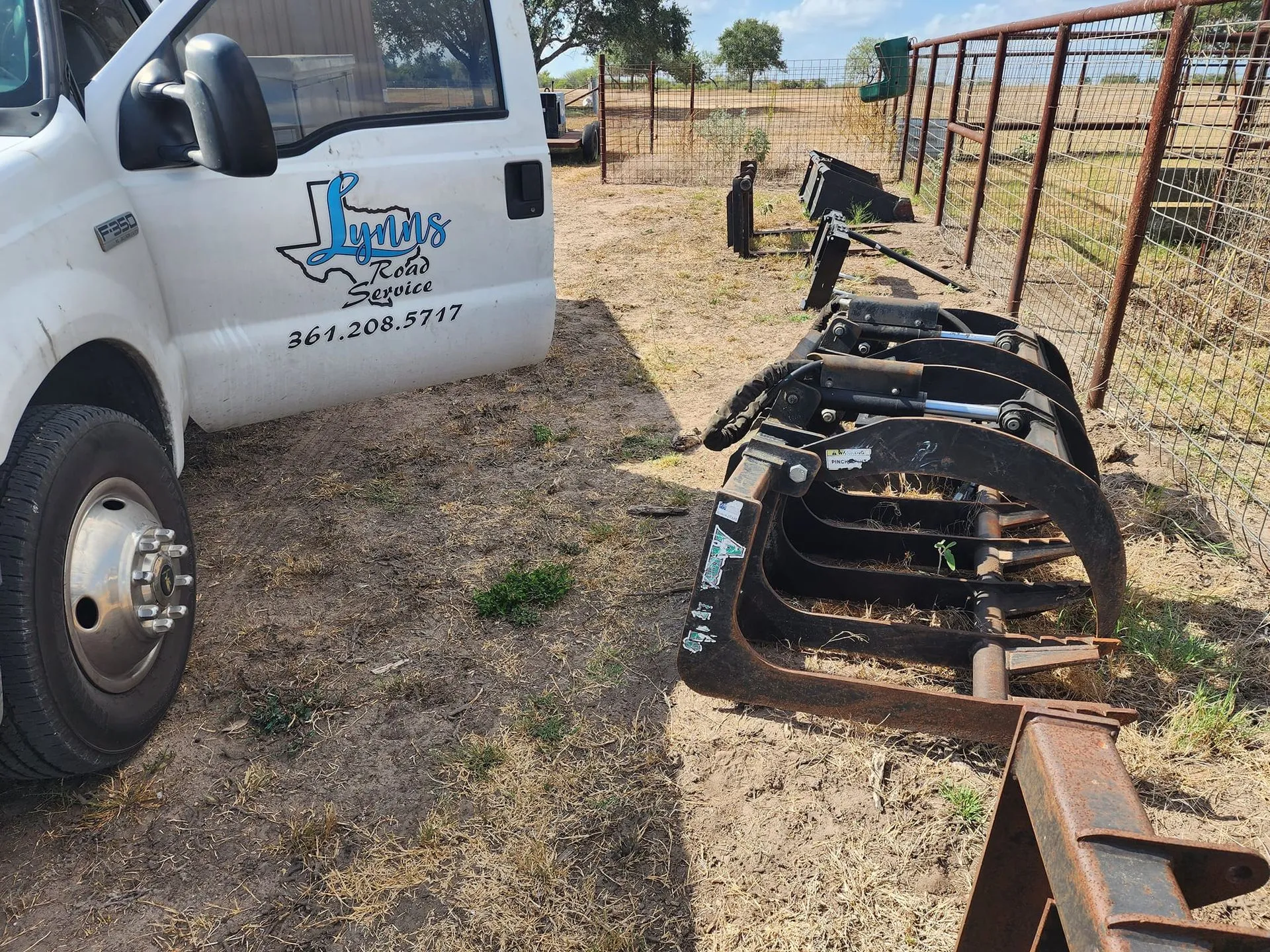 White truck parked near a black grapple lying on the grass.