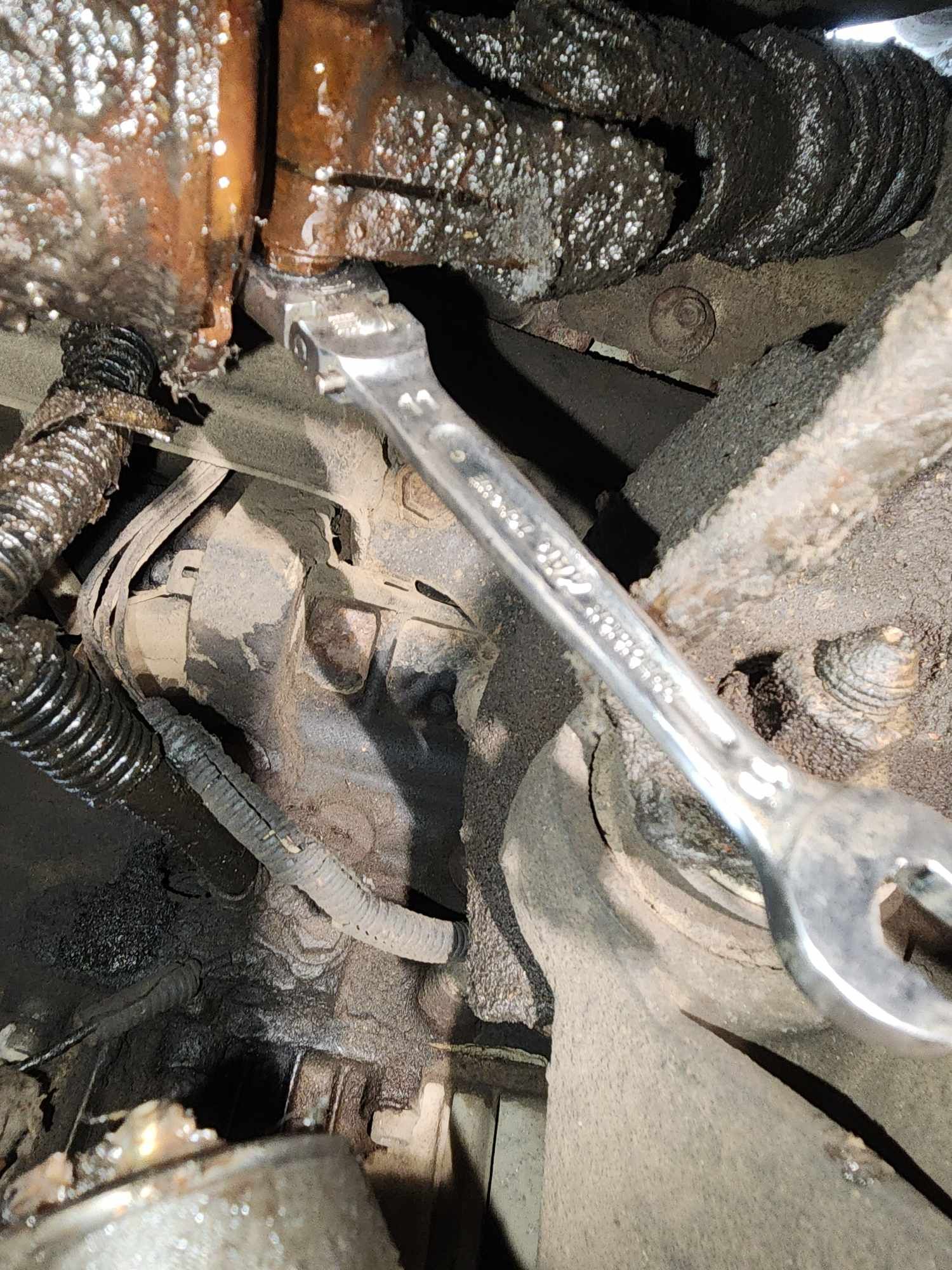 A wrench tightening a fitting on a greasy engine component.