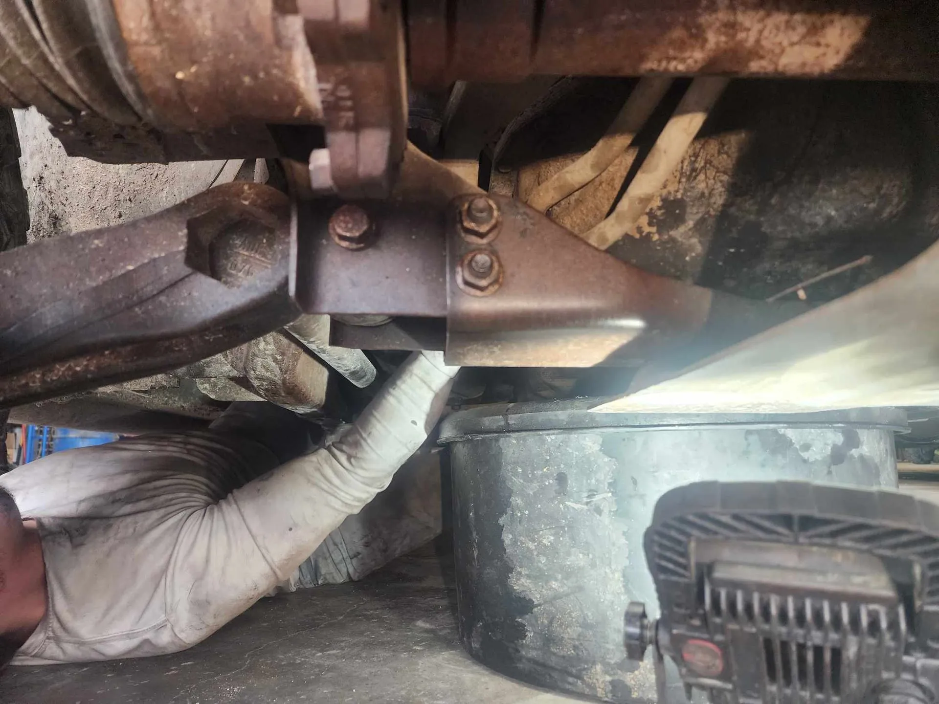Mechanic working on a vehicle's undercarriage with a wrench and drain pan.