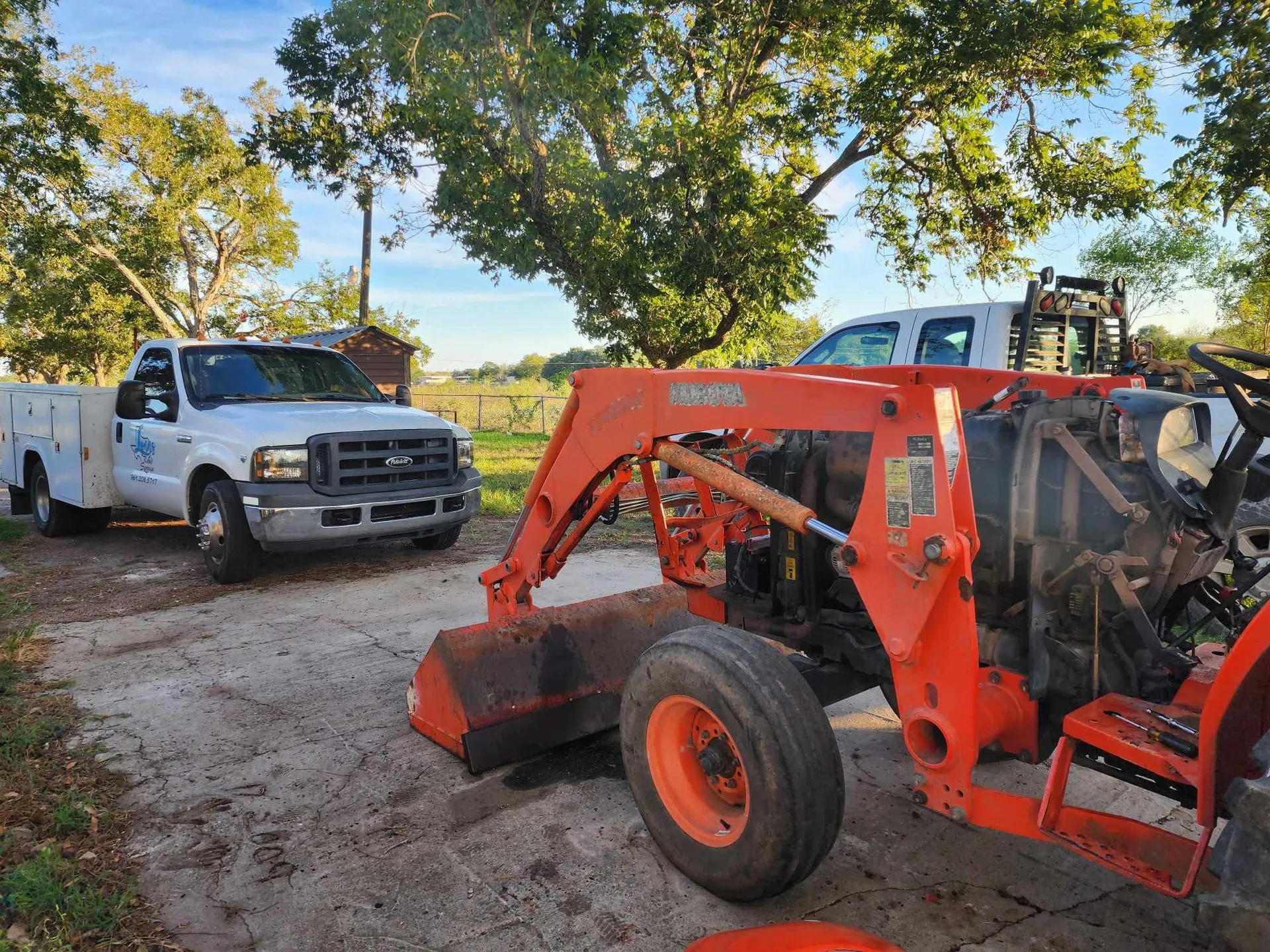 White truck and orange tractor parked outside during the day.