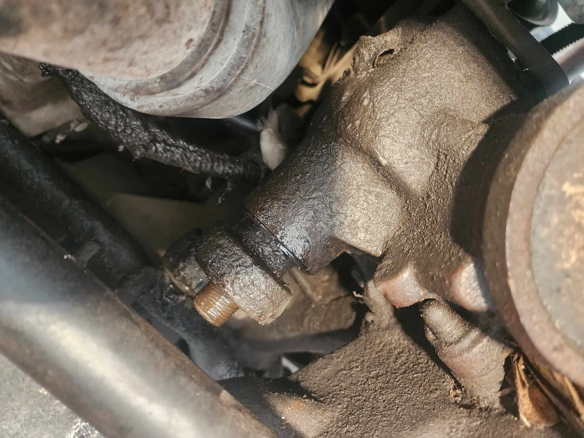 Engine component with an oil leak, covered in grime.
