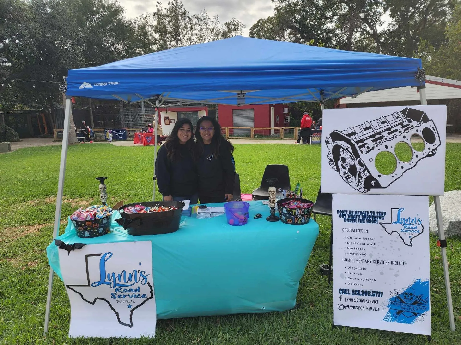 Two women at a Lynn's Road Service booth selling auto parts under a blue canopy.