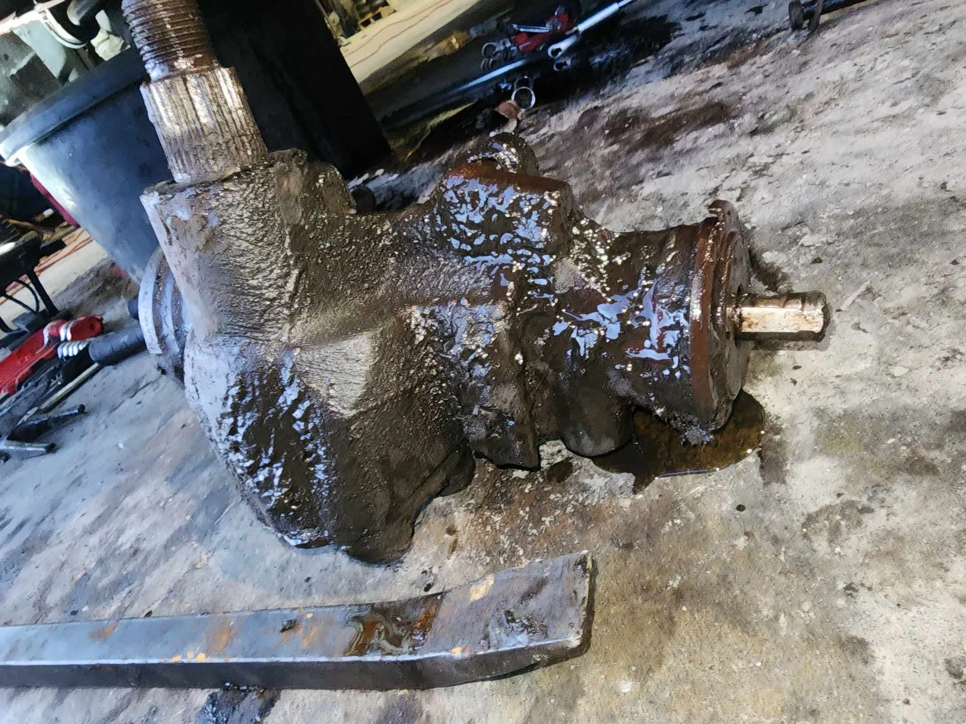 Greasy, rusty steering gear box on a concrete surface with a crowbar.