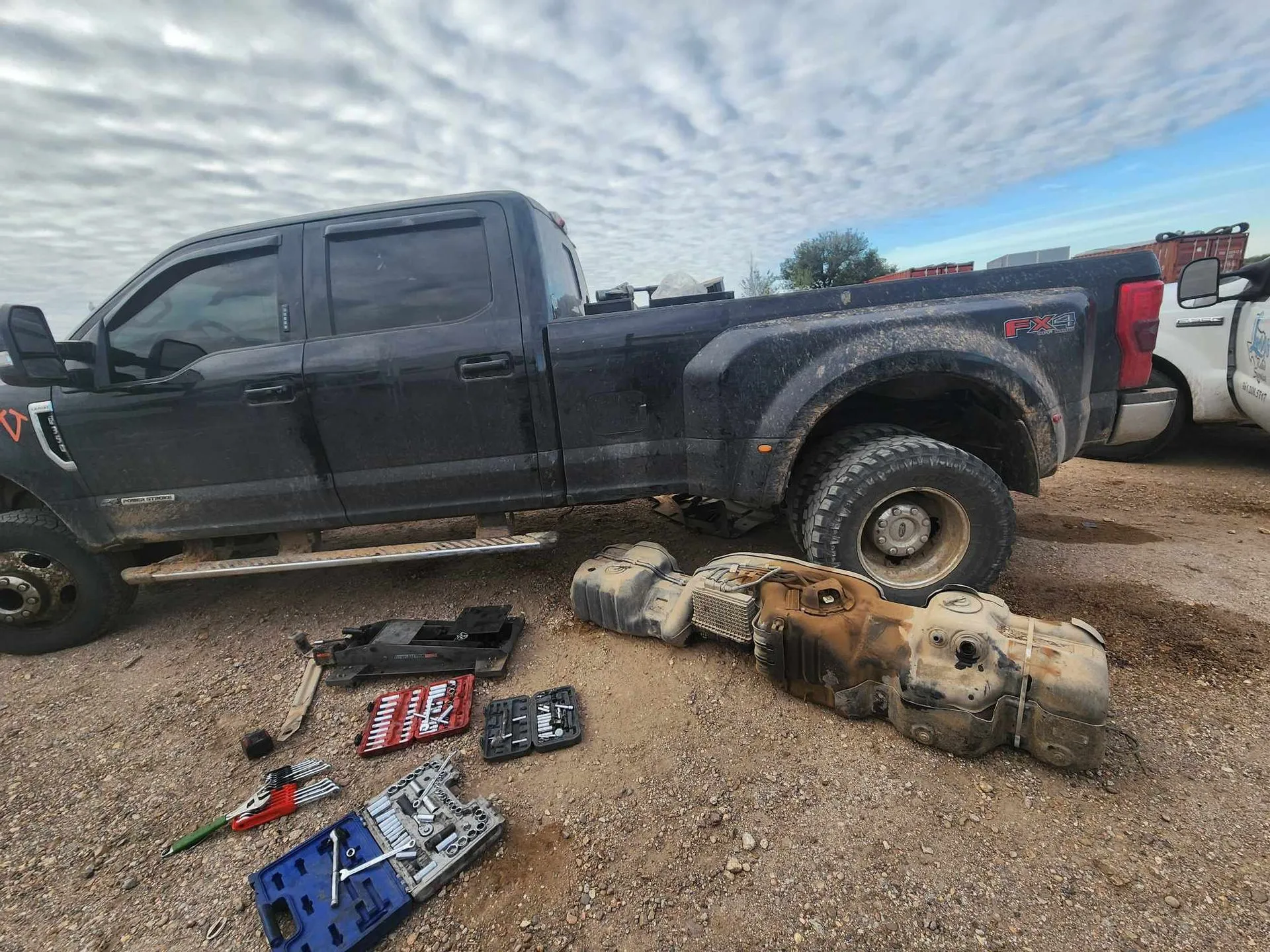 Black pickup truck with a detached fuel tank on a dirt surface.