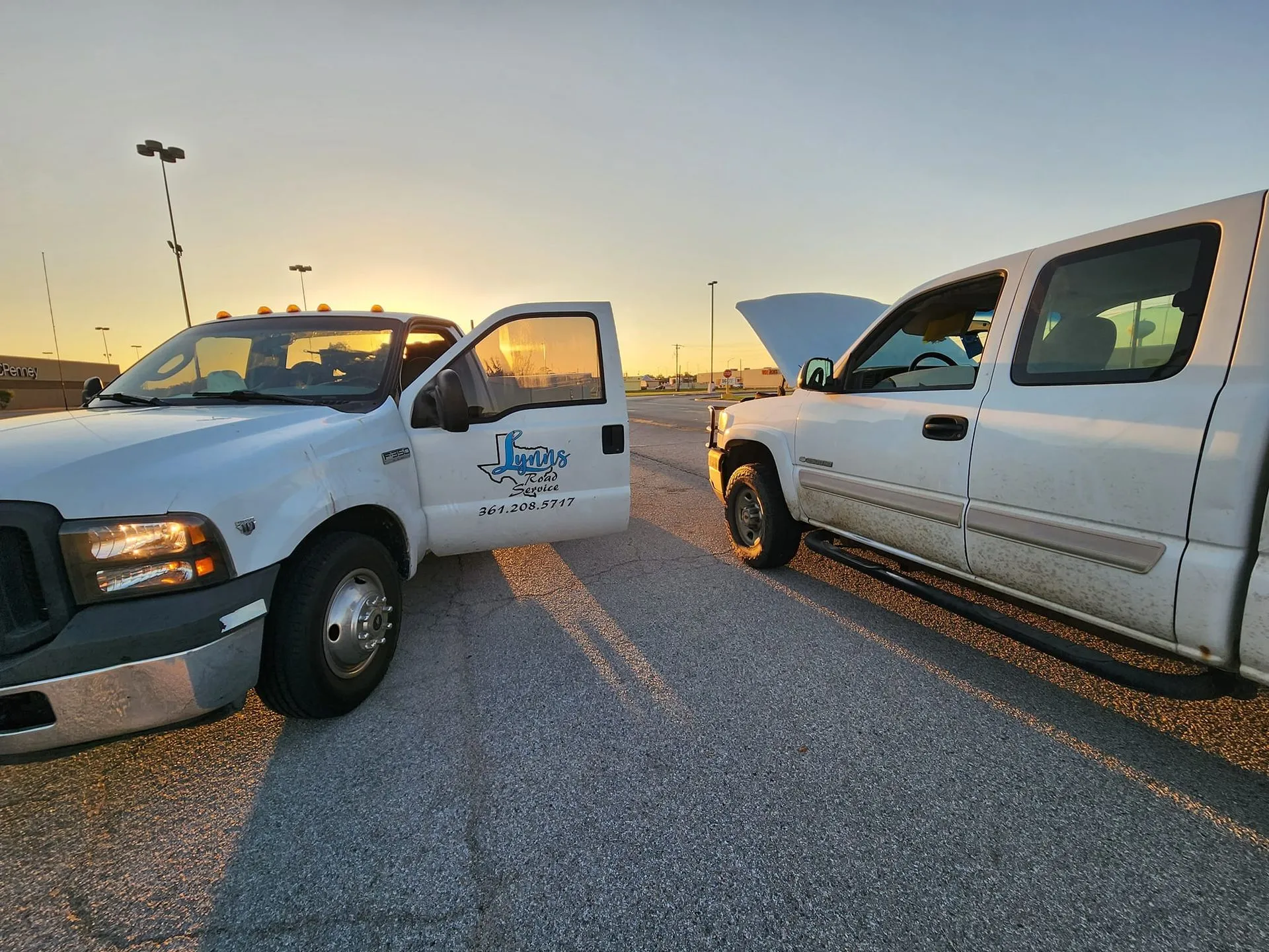 Two white Lynn's Road Service work trucks parked outdoors at sunset.