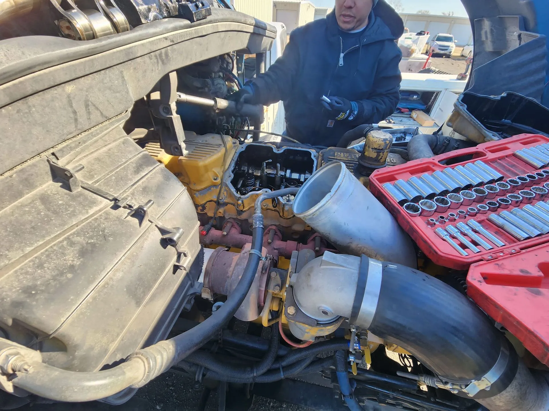 Mechanic working on a truck engine with tools laid out, outdoors.