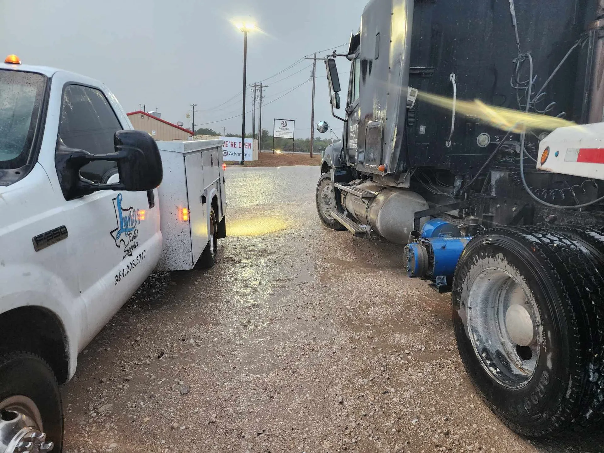 A service truck and a black semi-truck parked on a wet road at night.