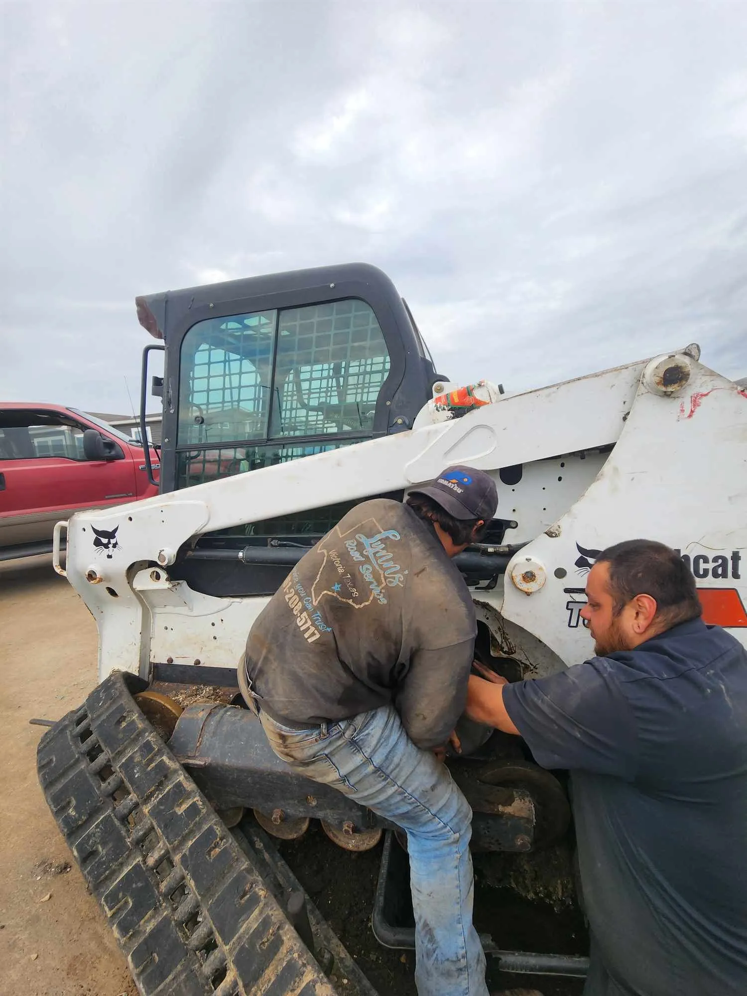 Two men working on a white Bobcat track loader outdoors.