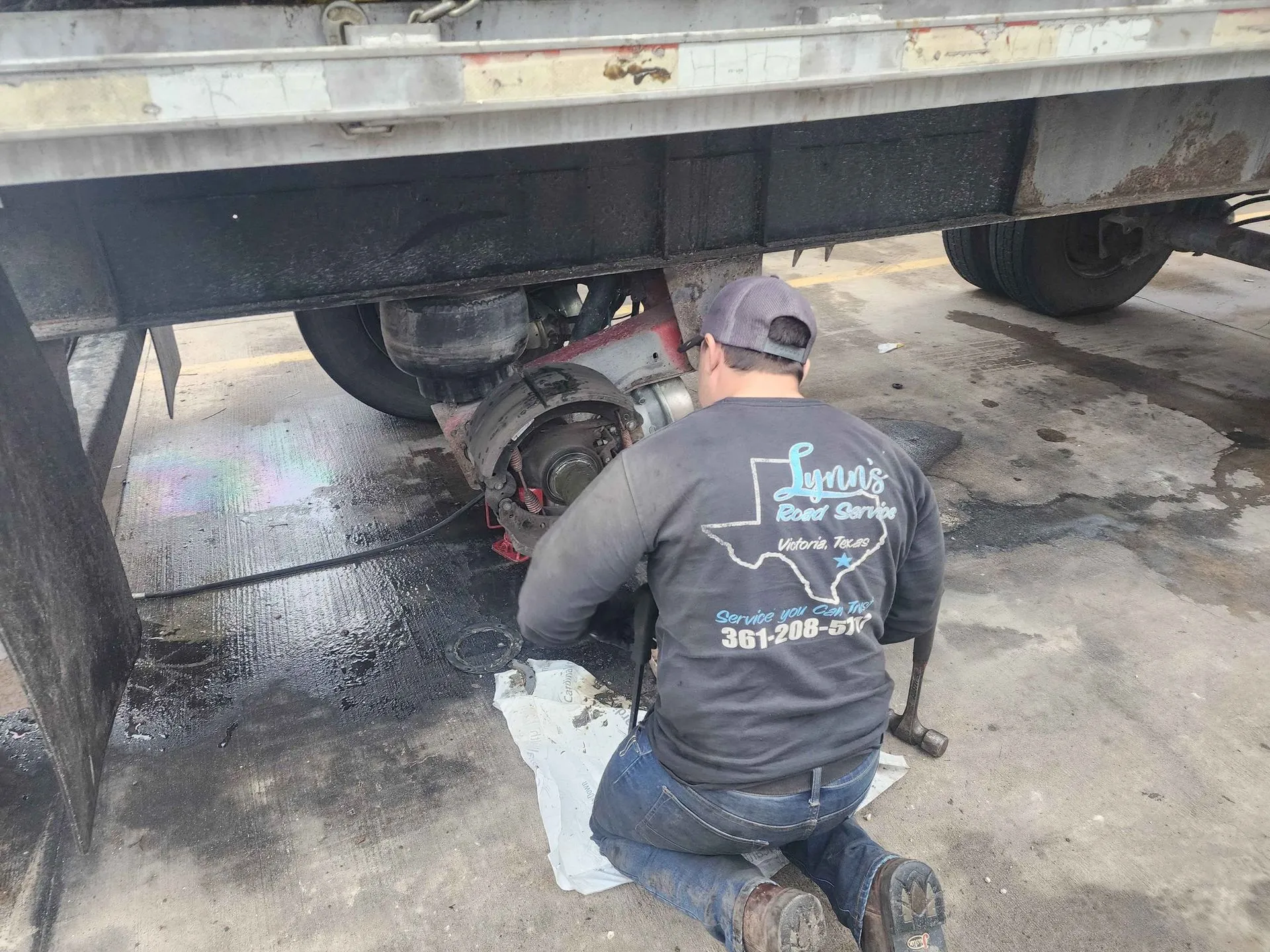 Mechanic repairing a truck axle on the ground.